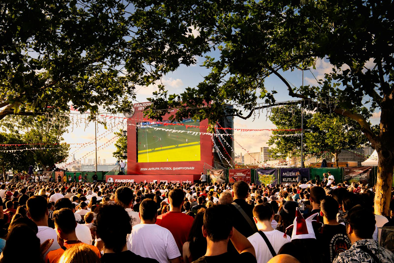 Fans gathered outdoors watching a football match on a giant public screen