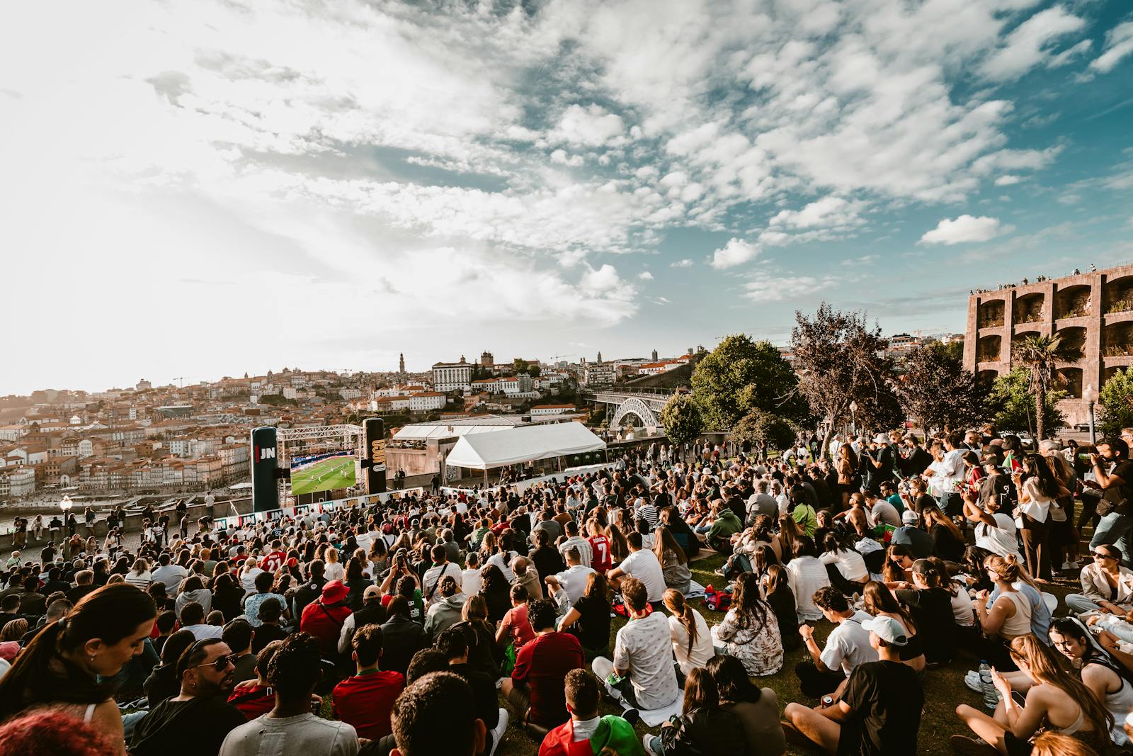 Fans gathered outdoors watching a football match on a giant public screen